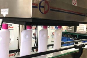 Bottles passing through an induction cap sealing machine on an automated packaging line.