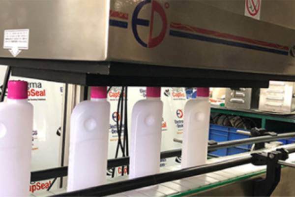 Bottles passing through an induction cap sealing machine on an automated packaging line.