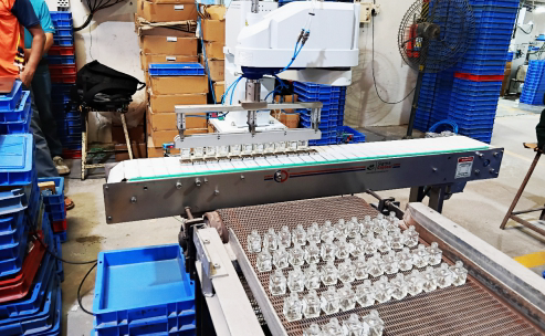 Cartesian gantry robot picking and placing clear plastic components from a conveyor in an industrial workspace.