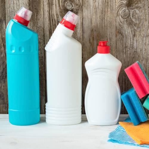 Three household cleaning product bottles with red caps displayed alongside colorful cleaning sponges on a wooden surface.