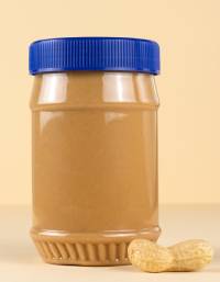Transparent plastic jar with a blue ribbed screw cap containing peanut butter, displayed alongside a peanut on a neutral background. The packaging highlights product protection and consumer convenience.