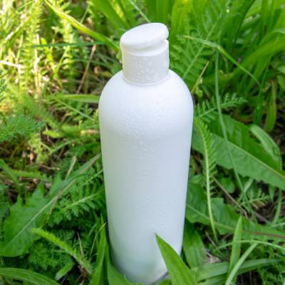 White plastic bottle with a flip-top dispensing closure placed outdoors among green vegetation, commonly used for agrochemical, crop protection, and agricultural liquid formulations.