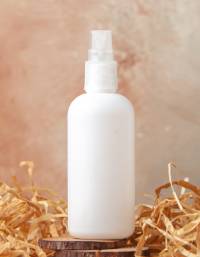 White plastic spray bottle displayed on a wooden surface with decorative straw packaging material in the background.