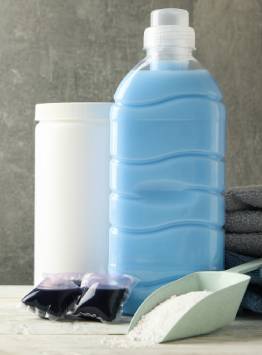 Large blue liquid detergent bottle displayed with detergent powder, laundry pods, and a refill container in a laundry care setting.