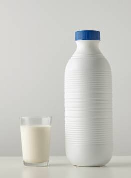 White plastic milk bottle with a blue screw cap placed beside a glass of milk.