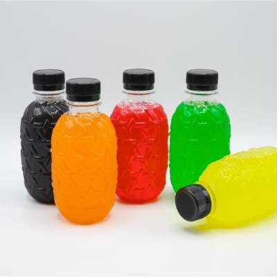 Five transparent plastic beverage bottles filled with brightly colored drinks in black, orange, red, green, and yellow, each sealed with a black screw-on cap. The bottles feature textured sidewalls and are displayed against a neutral background.