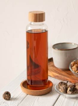 Clear beverage bottle filled with amber-colored liquid and fitted with a wooden screw-cap closure.